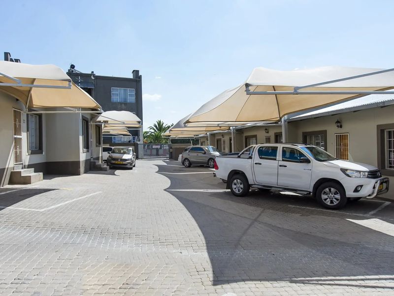 Exterior view of a townhouse complex driveway featuring paved parking areas and installed shade cloth carports for vehicle protection.