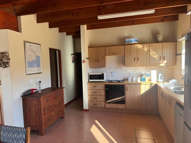 A functional kitchen featuring light wood cabinetry, exposed timber ceiling beams, tiled flooring, and a built-in oven with hob.