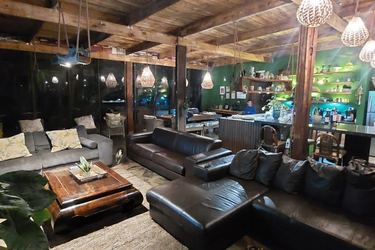 Spacious open-plan living and kitchen area featuring exposed timber ceiling beams, concrete flooring, and a functional kitchen island with open shelving.