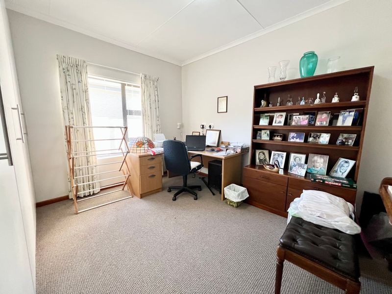 A functional home office space featuring neutral carpeting, built-in cupboard storage, and a window with natural light.