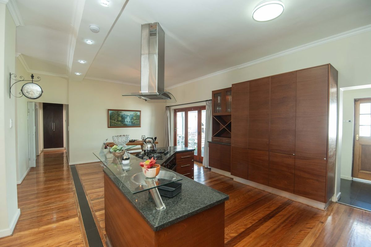 Modern kitchen featuring a central island with granite countertop, stainless steel extractor fan, extensive built-in cabinetry, and polished hardwood flooring.