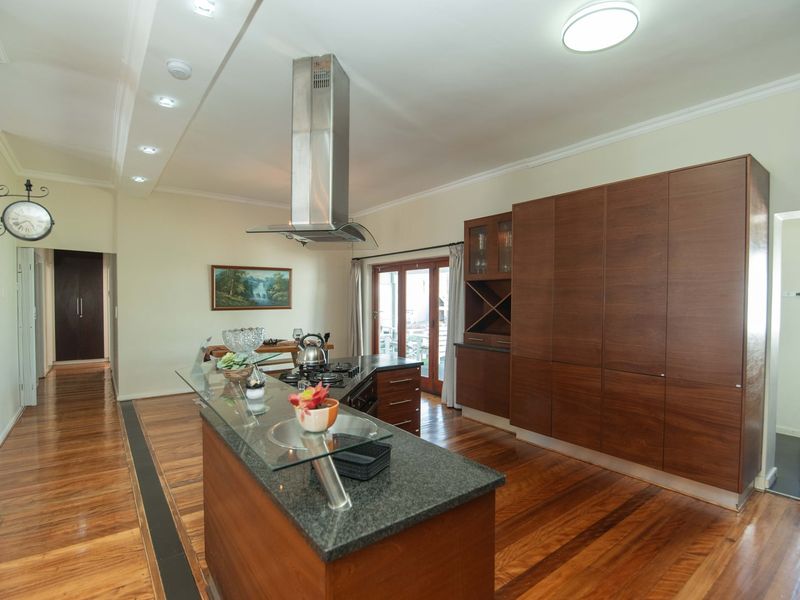 Modern kitchen featuring a central island with granite countertop, stainless steel extractor fan, extensive built-in cabinetry, and polished hardwood flooring.