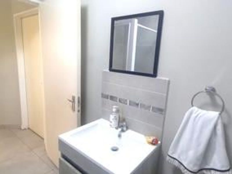 A clean bathroom featuring a modern vanity basin with a tiled splashback, wall-mounted mirror, and neutral floor tiling.