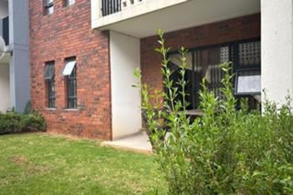 Rear view of the apartment building featuring a face brick facade, a ground floor patio area, and a small private lawn.