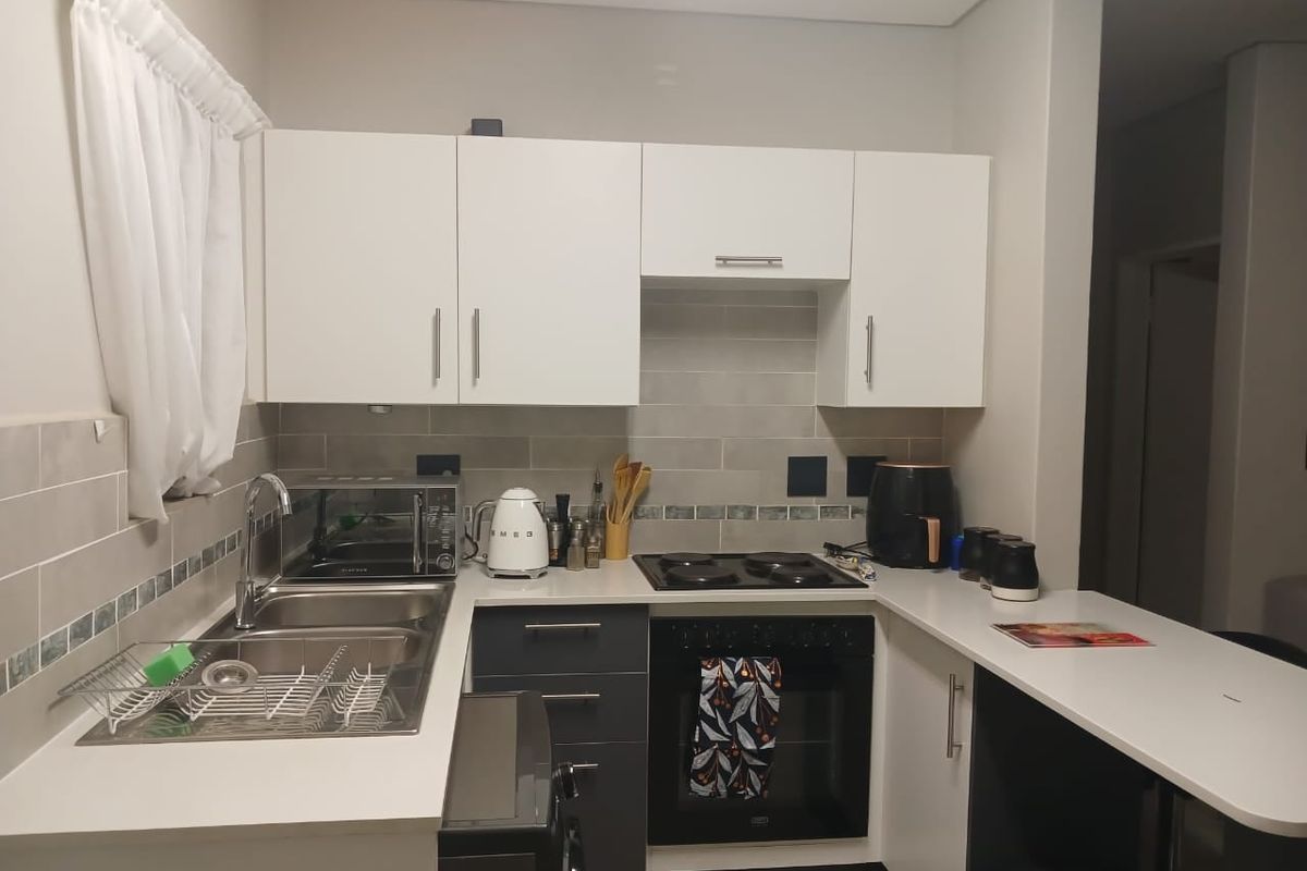 A functional kitchen featuring modern white and dark grey cabinetry, stone countertops, a built-in oven, electric hob, and a stainless steel sink.