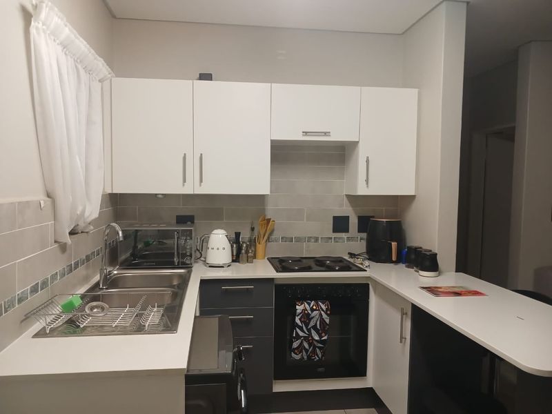 A functional kitchen featuring modern white and dark grey cabinetry, stone countertops, a built-in oven, electric hob, and a stainless steel sink.