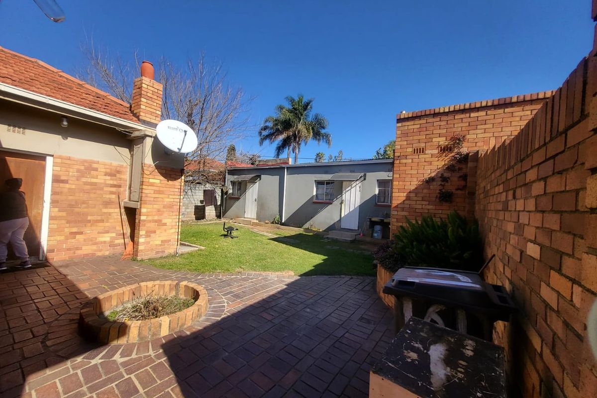 A rear garden area featuring a brick-paved patio, a built-in fire pit, and a separate outbuilding, enclosed by brick boundary walls.