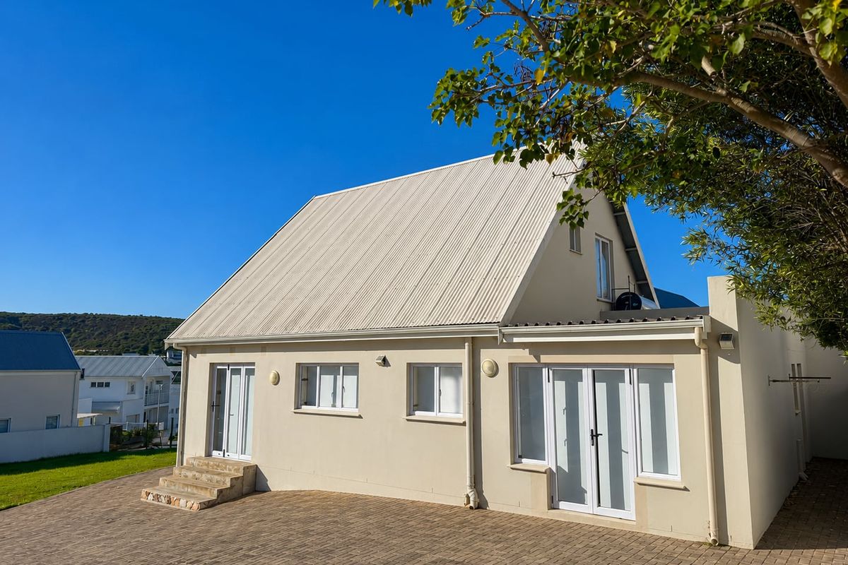 Rear view of a well-maintained house featuring a corrugated metal roof, paved patio area, and multiple glass door and window access points.