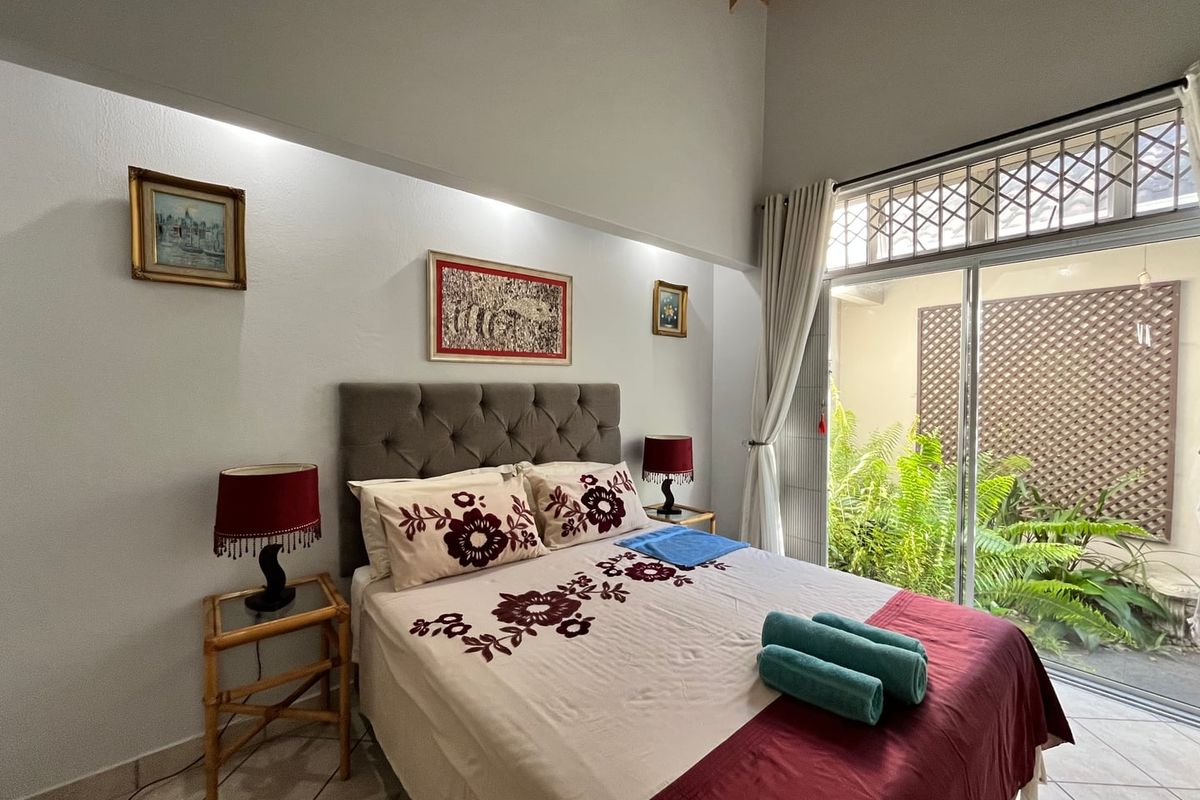 A well-lit bedroom featuring high vaulted ceilings, tiled flooring, and large sliding glass doors providing direct access to a private garden area.