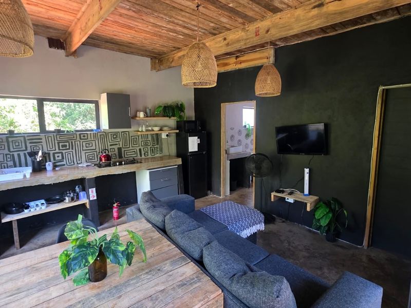 Open-plan living area featuring an exposed timber beam ceiling, concrete kitchen countertops with patterned backsplash, and polished concrete flooring in a lodge-style setting.