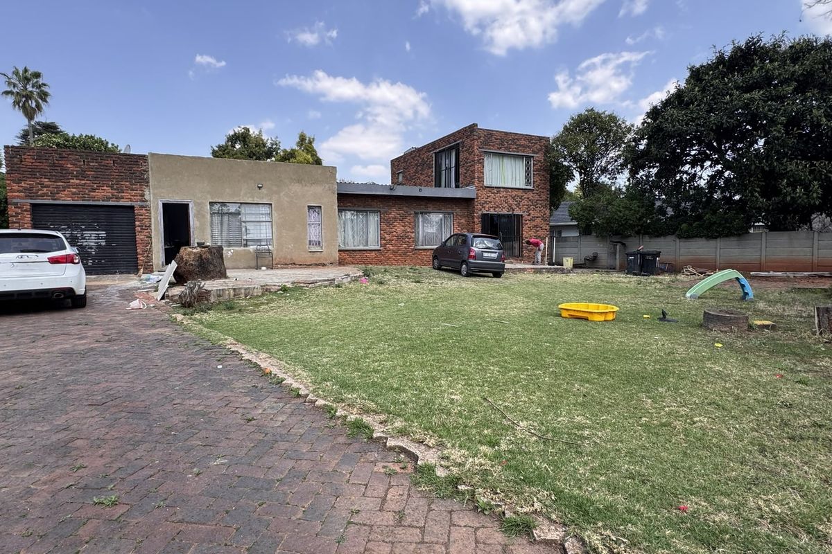 Rear view of a multi-level brick house featuring a paved driveway, large lawn area, and perimeter boundary wall.
