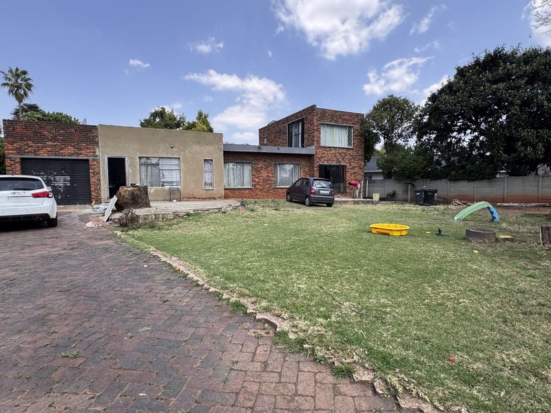 Rear view of a multi-level brick house featuring a paved driveway, large lawn area, and perimeter boundary wall.