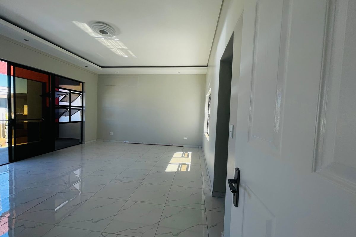A bright, empty living room featuring modern white marble-look floor tiles, recessed ceiling lighting, and a large sliding glass door leading to an outdoor area.