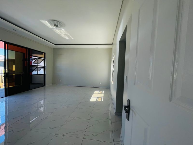 A bright, empty living room featuring modern white marble-look floor tiles, recessed ceiling lighting, and a large sliding glass door leading to an outdoor area.