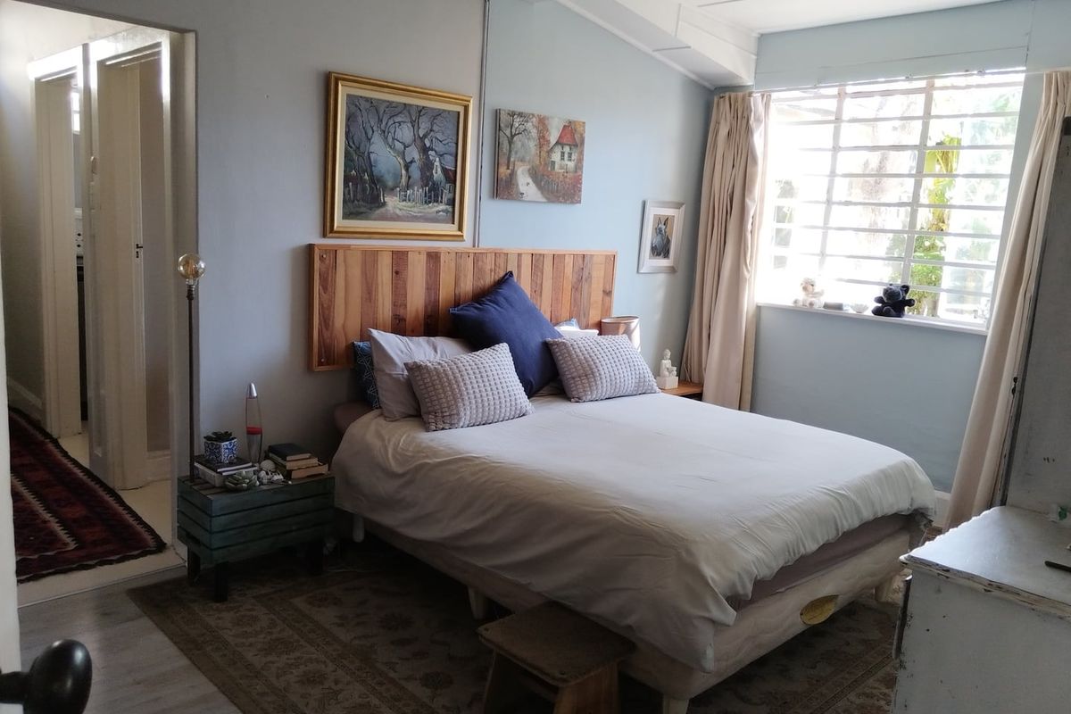 A bedroom featuring a timber headboard, laminate flooring, and a large steel-framed window allowing natural light into the space.