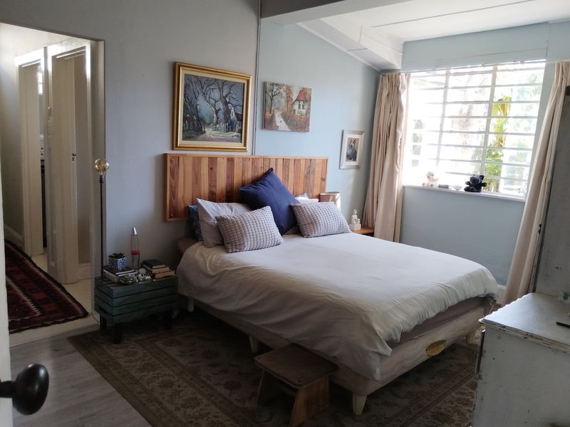 A bedroom featuring a timber headboard, laminate flooring, and a large steel-framed window allowing natural light into the space.