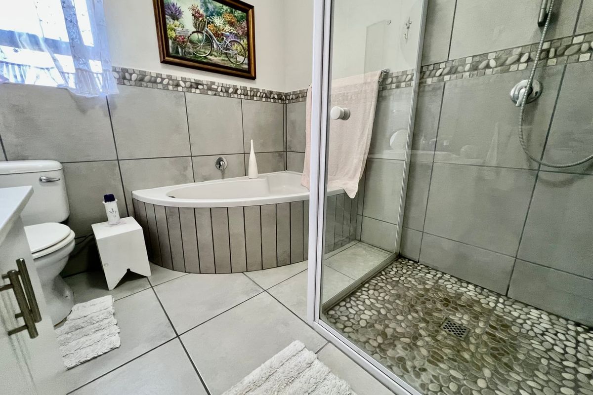 A well-maintained bathroom featuring a corner bathtub, a separate glass-enclosed shower with pebble flooring, and neutral ceramic tiling throughout.