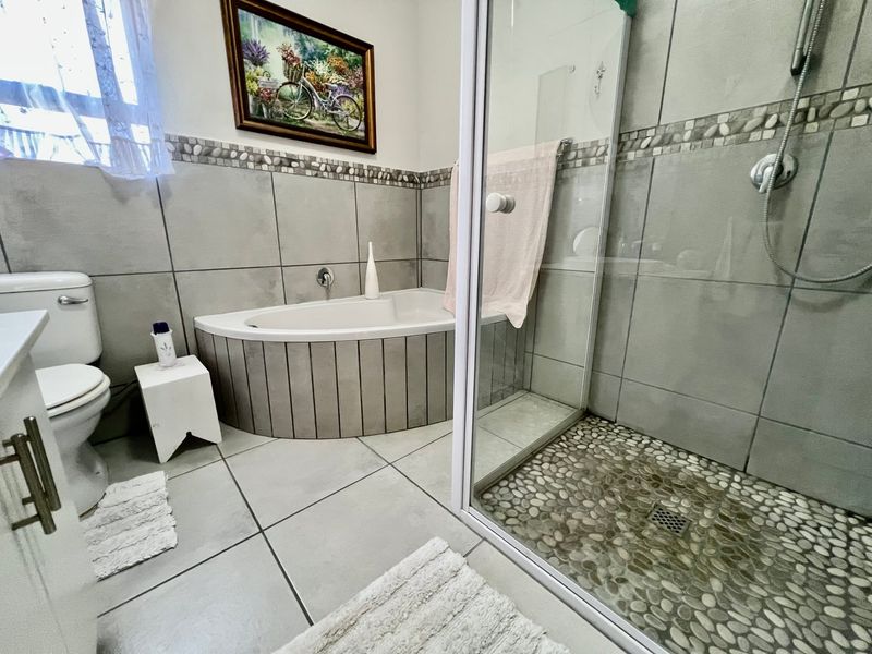A well-maintained bathroom featuring a corner bathtub, a separate glass-enclosed shower with pebble flooring, and neutral ceramic tiling throughout.