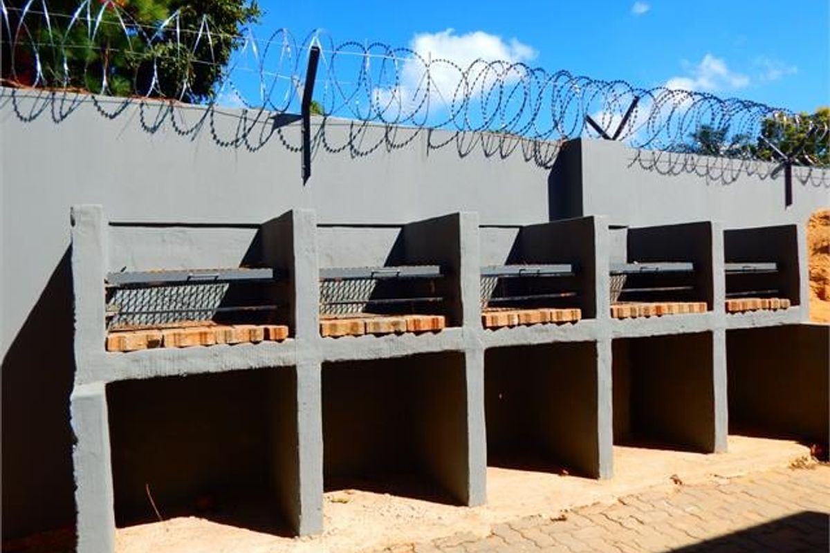 Outdoor communal braai area featuring multiple built-in masonry barbecue stations against a perimeter wall with security razor wire.