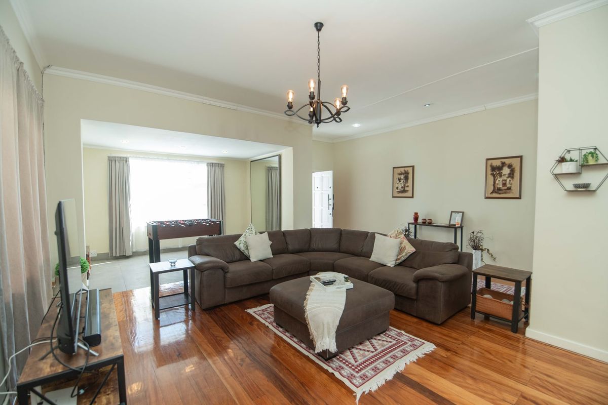 Spacious living room featuring polished hardwood flooring, elegant crown molding, and a classic wrought iron chandelier, creating a warm and inviting atmosphere.