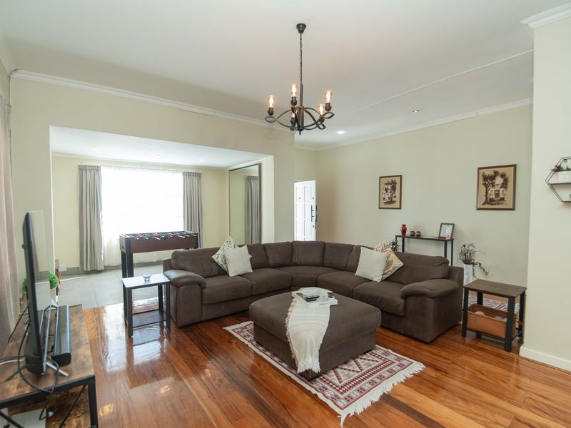 Spacious living room featuring polished hardwood flooring, elegant crown molding, and a classic wrought iron chandelier, creating a warm and inviting atmosphere.