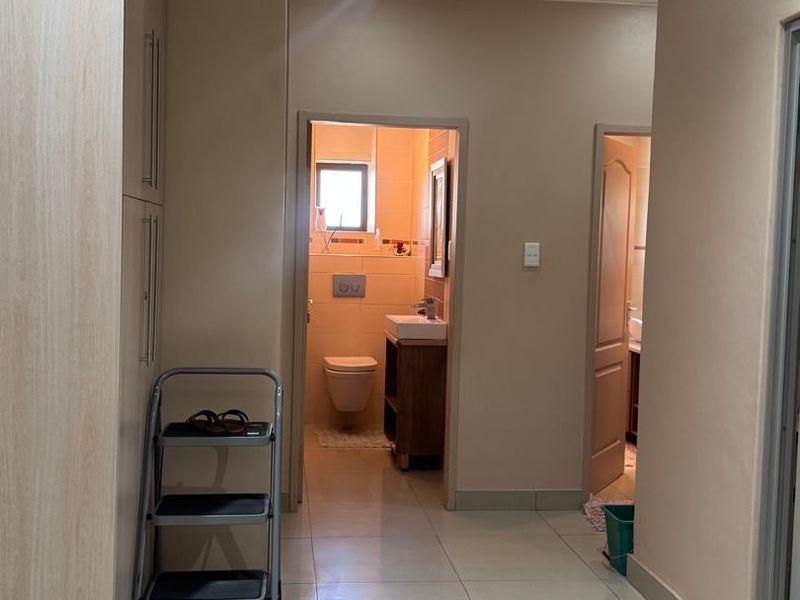 A clean, tiled hallway featuring built-in cabinetry and direct access to a bathroom, providing a functional and well-maintained transition space within the apartment.