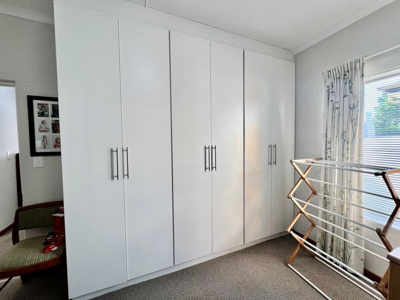 A bedroom featuring floor-to-ceiling white built-in cupboards and neutral carpeting, providing ample storage space.