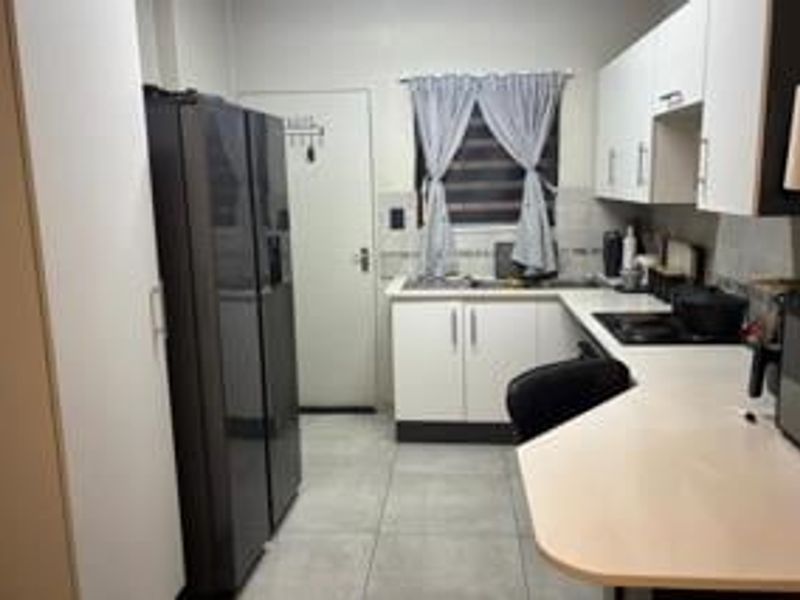 A functional kitchen featuring white cabinetry, laminate countertops, tiled flooring, and a built-in hob, providing a practical workspace for daily cooking.