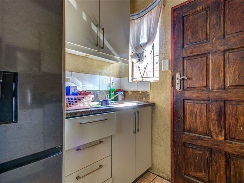 A compact scullery area featuring built-in cabinetry, a stainless steel sink, and a solid wood door, requiring some wall maintenance.