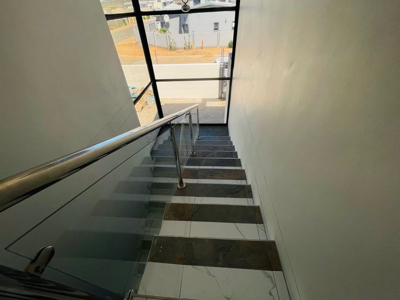 A modern staircase featuring a glass balustrade with a stainless steel handrail and contrasting tiled steps, illuminated by a large window.
