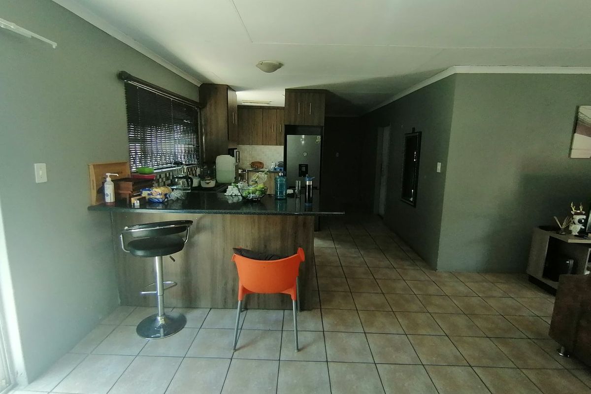 Open plan living area featuring a kitchen with built-in cabinetry, granite countertops, and a breakfast bar, finished with tiled flooring throughout.