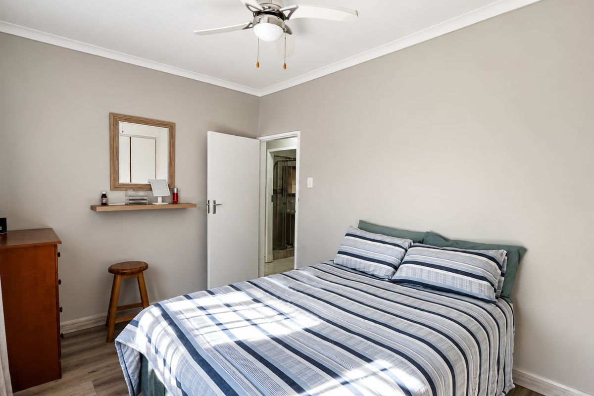 A well-lit bedroom featuring neutral wall tones, a ceiling fan, and direct access to an en-suite bathroom.