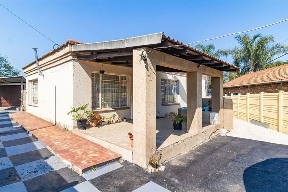 Rear exterior view featuring a covered patio area with concrete pillars, tiled flooring, and access to the paved driveway and garden space.