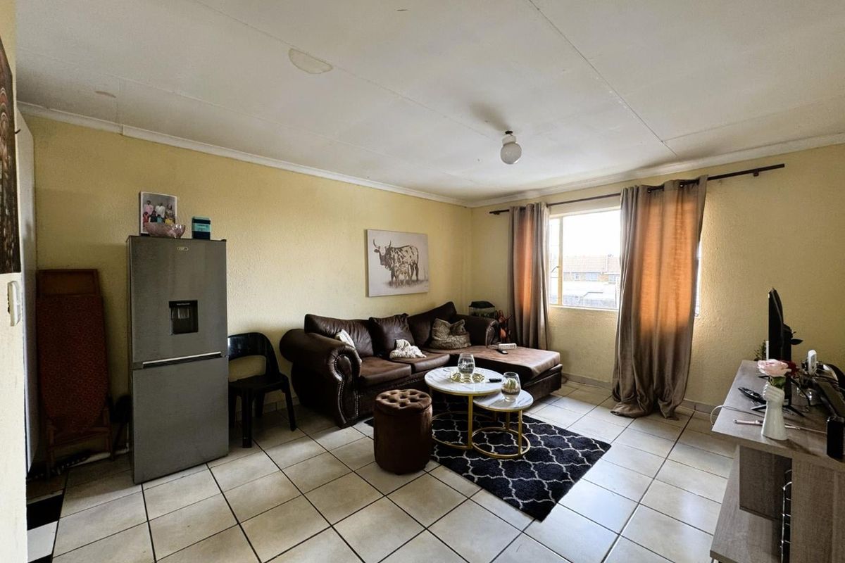 A living room featuring tiled flooring and a large window, providing a functional space with potential for cosmetic updates.