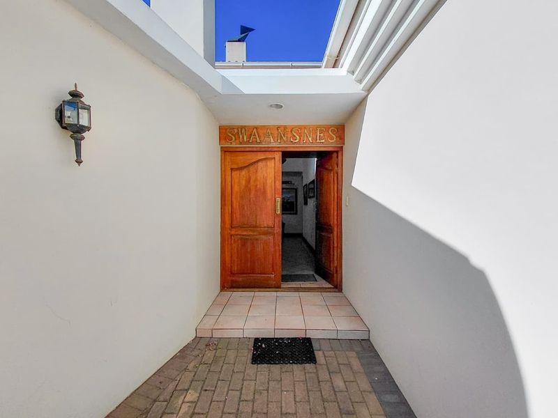 A welcoming front entrance featuring a solid wooden double door, paved walkway, and a tiled step leading into the home.