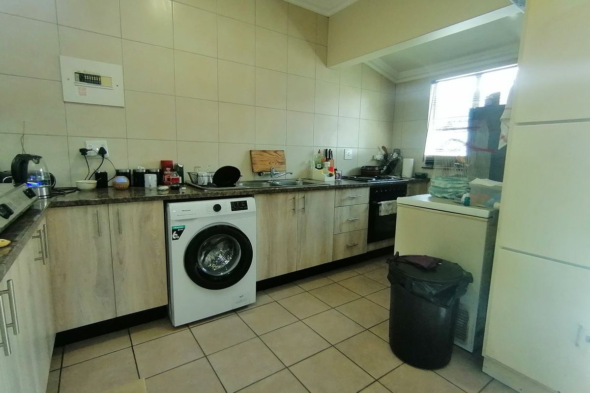 Functional kitchen featuring light wood-finish cabinetry, tiled splashbacks, integrated oven and hob, and dedicated space for laundry appliances.