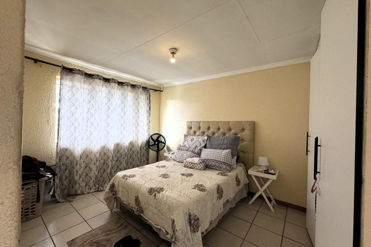 A functional bedroom featuring tiled flooring, built-in wardrobe storage, and a window with curtain fixtures.