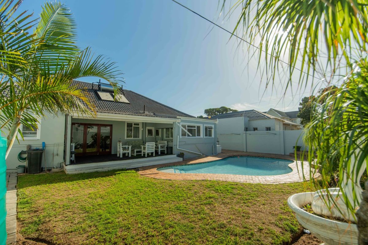 Rear exterior view featuring a swimming pool with paved surround, a covered patio area, and a solar water heating system on the tiled roof.