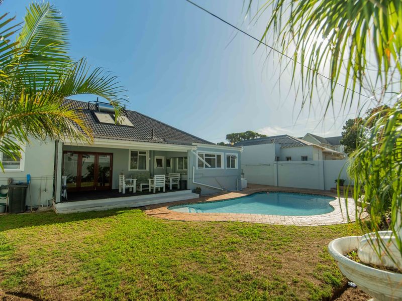 Rear exterior view featuring a swimming pool with paved surround, a covered patio area, and a solar water heating system on the tiled roof.