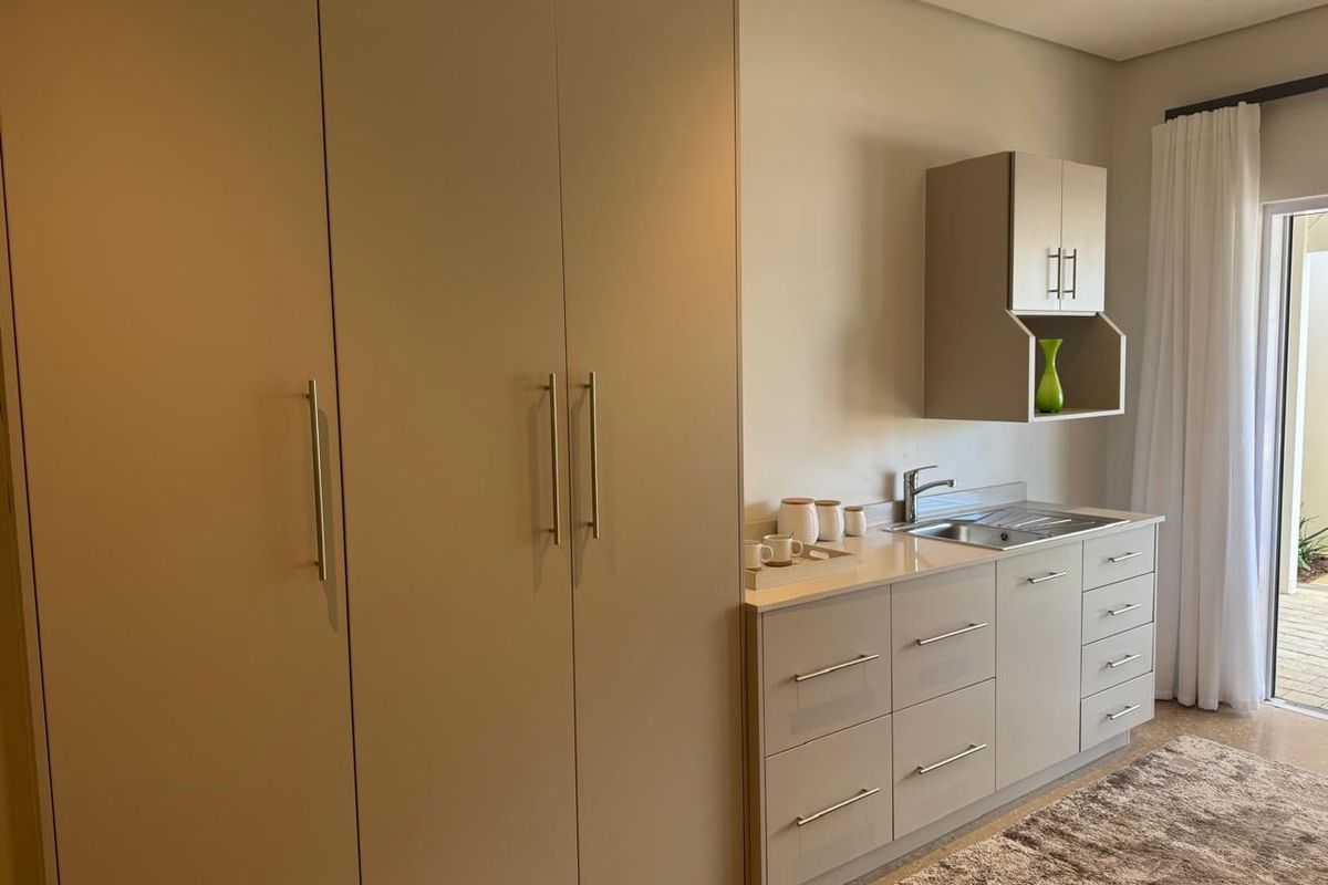 A modern kitchenette featuring sleek built-in cabinetry, stone countertops, a stainless steel sink, and direct access to an outdoor patio area.