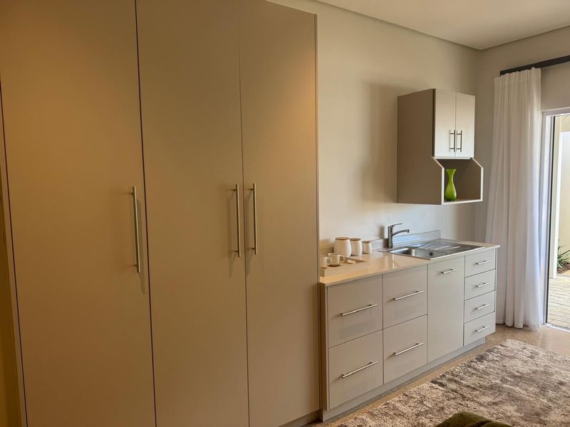 A modern kitchenette featuring sleek built-in cabinetry, stone countertops, a stainless steel sink, and direct access to an outdoor patio area.