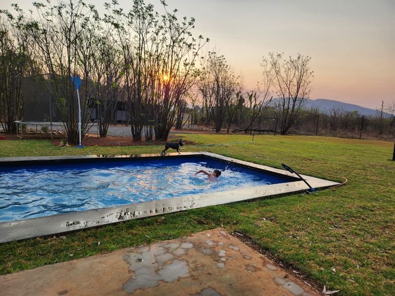 Outdoor swimming pool area set within a spacious garden, featuring a concrete pool surround and scenic sunset views.