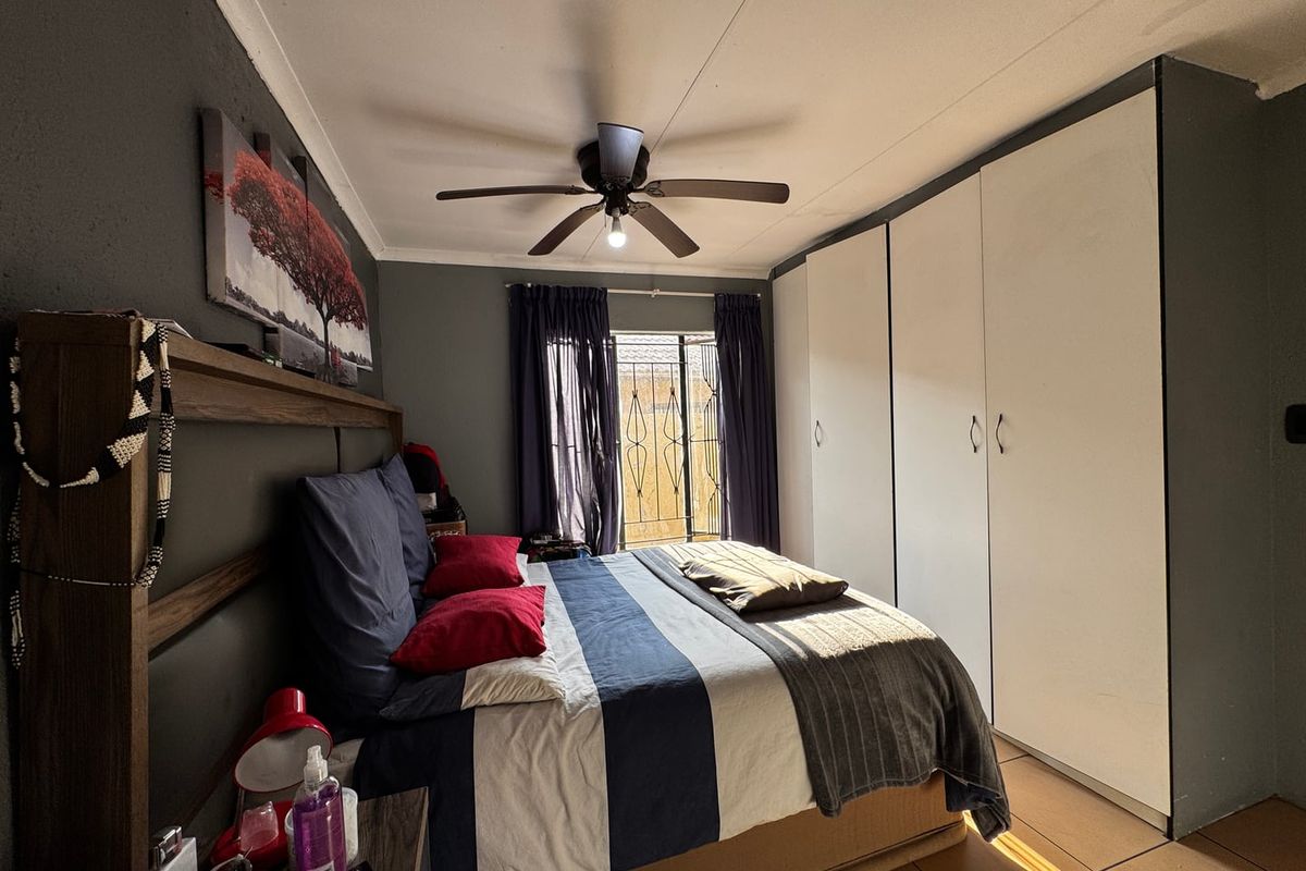 A bedroom featuring built-in wardrobes, a ceiling fan, and tiled flooring with access to an exterior area through a security gate.