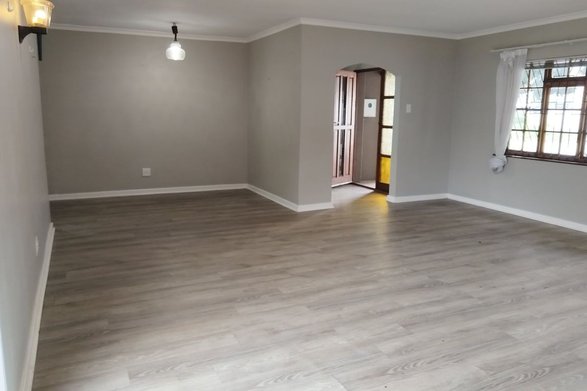A spacious, empty living room featuring modern grey laminate flooring, neutral walls, an arched doorway, and a classic timber-framed window.