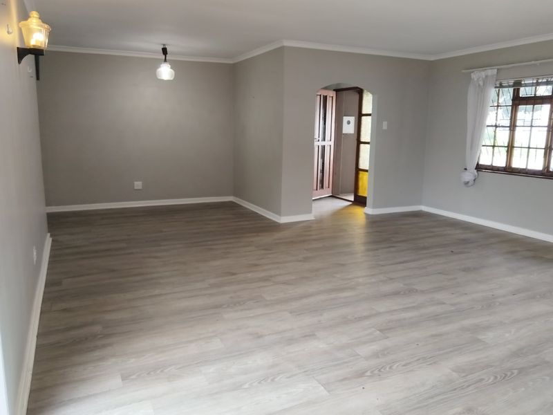 A spacious, empty living room featuring modern grey laminate flooring, neutral walls, an arched doorway, and a classic timber-framed window.