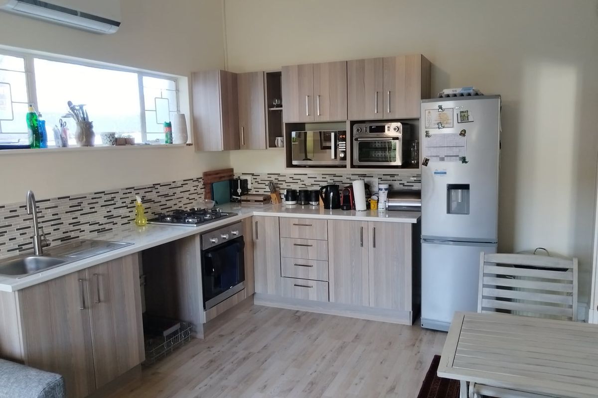 A functional kitchen featuring light wood-tone cabinetry, mosaic tile backsplash, built-in oven, gas hob, and laminate flooring with an integrated air conditioning unit.