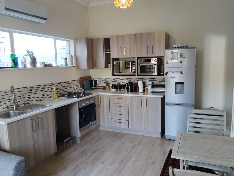 A functional kitchen featuring light wood-tone cabinetry, mosaic tile backsplash, built-in oven, gas hob, and laminate flooring with an integrated air conditioning unit.