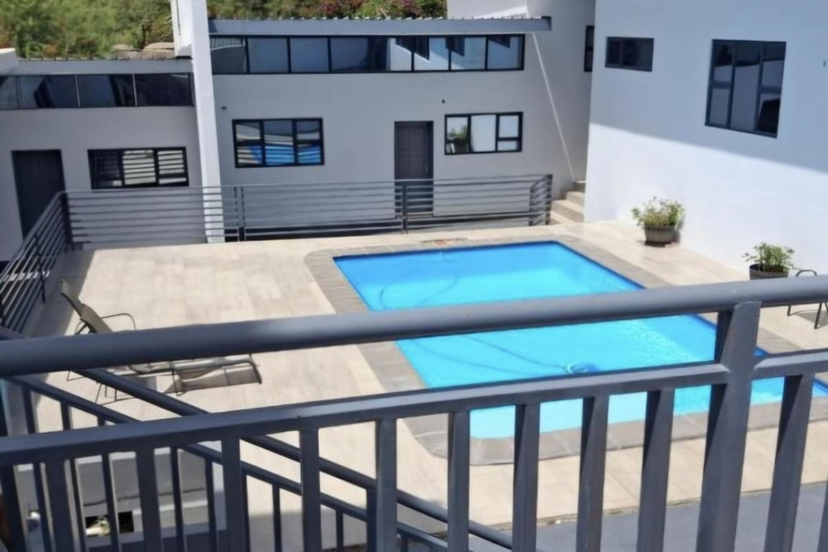 A well-maintained outdoor pool area featuring a tiled deck, modern metal balustrades, and a multi-level building facade with large windows.