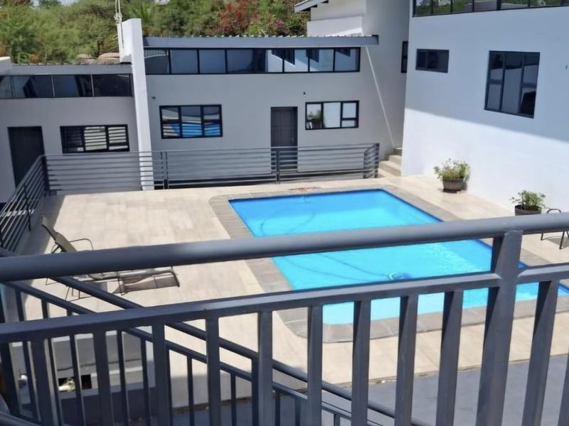 A well-maintained outdoor pool area featuring a tiled deck, modern metal balustrades, and a multi-level building facade with large windows.