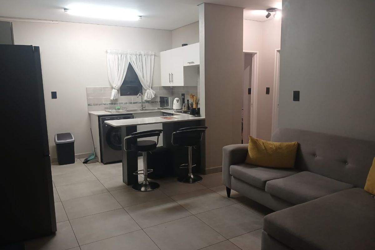 Open-plan living area featuring a compact kitchen with built-in cabinetry, a breakfast bar, and tiled flooring throughout the space.